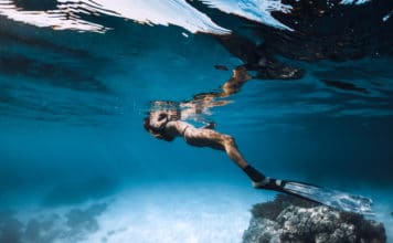 Woman freediver relax over sandy sea with fins. Underwater in blue ocean