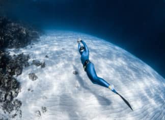 Woman freediver in monofin glides in the depth over the sandy bottom and looks at the surface